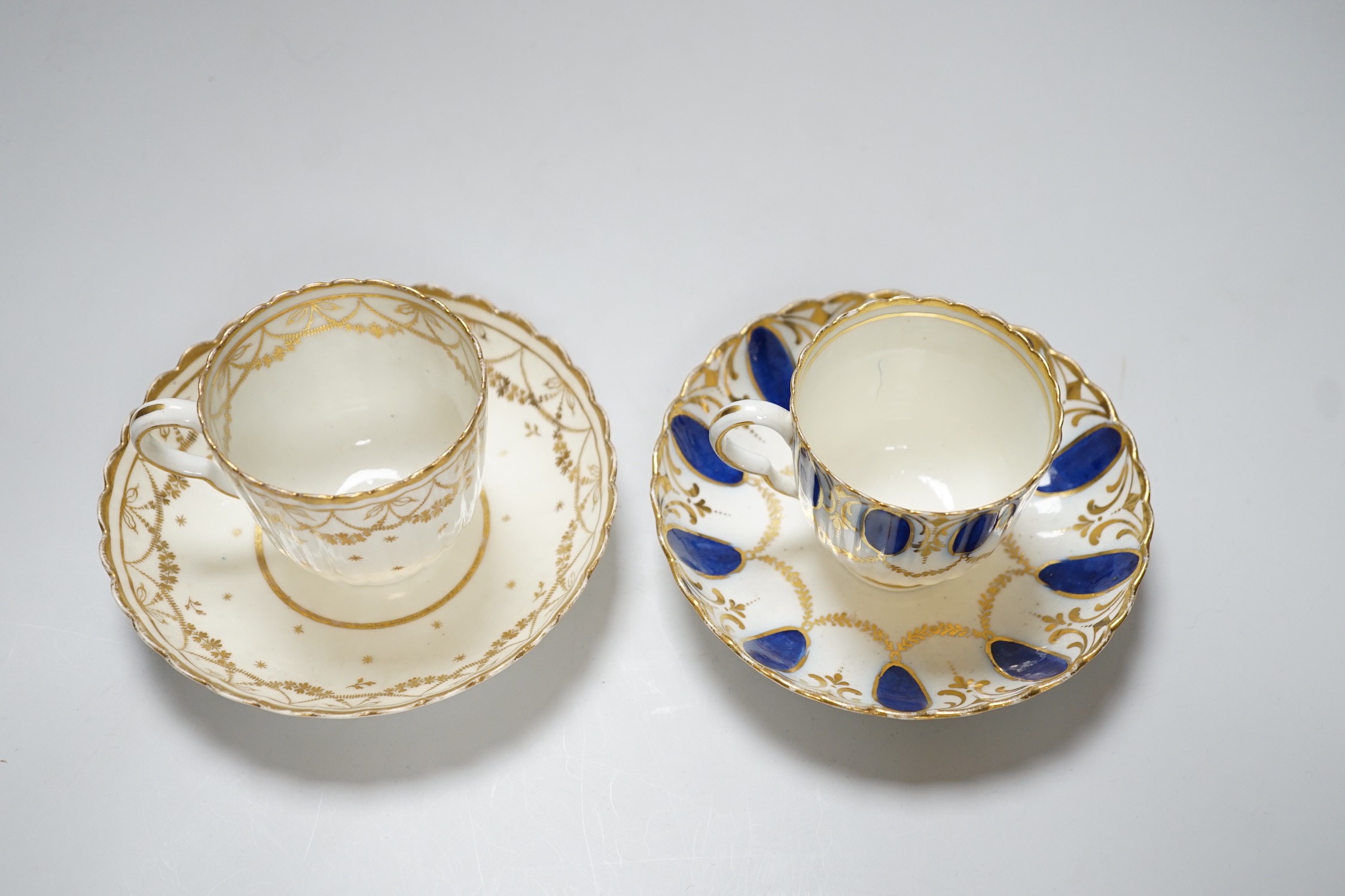 An 18th century Caughley coffee cup and saucer with blue pendants from gilt leafy swags and an 18th century Caughley coffee cup and saucer with an elaborately gilded border, both probably decorated at Chamberlains premis